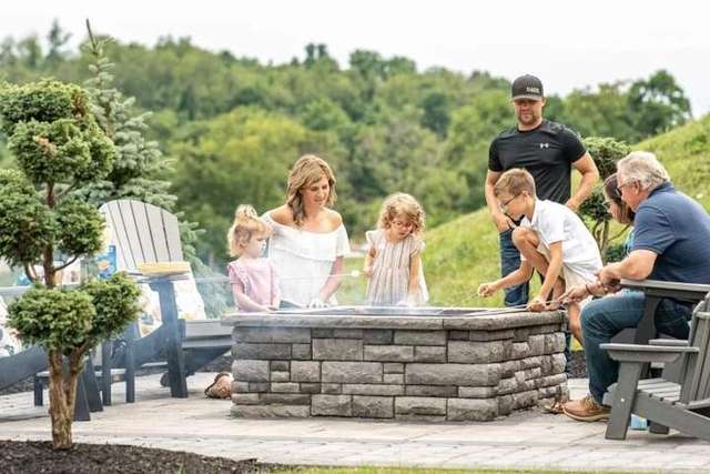A family gathers around a fire pit outdoors, roasting marshmallows and enjoying time together. – Palm Beach Outdoor Contracting