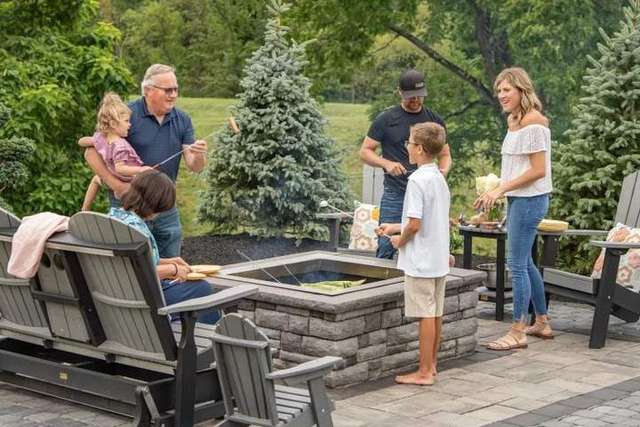 A family gathers around a backyard fire pit, roasting marshmallows and enjoying time together outdoors. – Palm Beach Outdoor Contracting