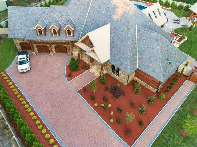 Aerial view of a large house with a driveway, parked white vehicle, and landscaped front yard. – Palm Beach Outdoor Contracting