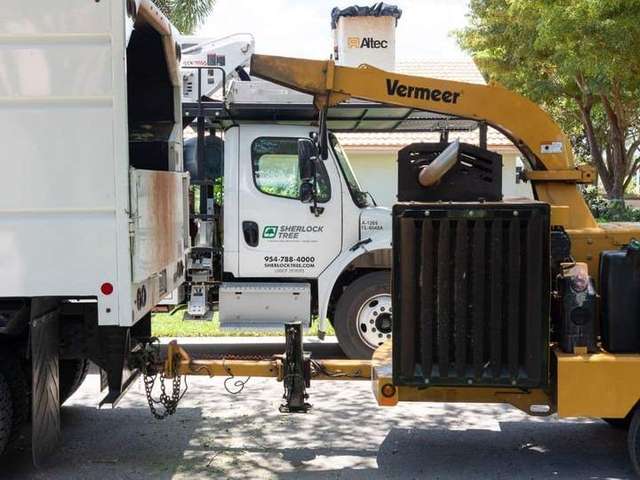 Sherlock Tree Company Altec bucket truck with a yellow Vermeer wood chipper set up on a residential street in South Flor – Sherlock Tree Company